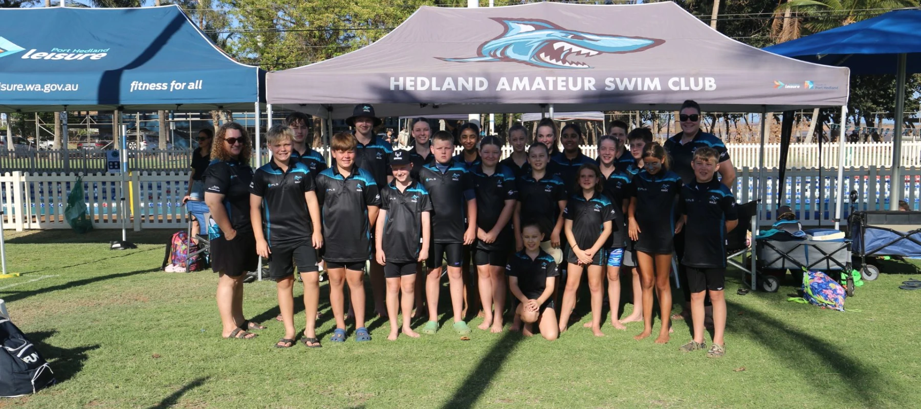 Group of young swim club members standing in front of marquee at a community pool