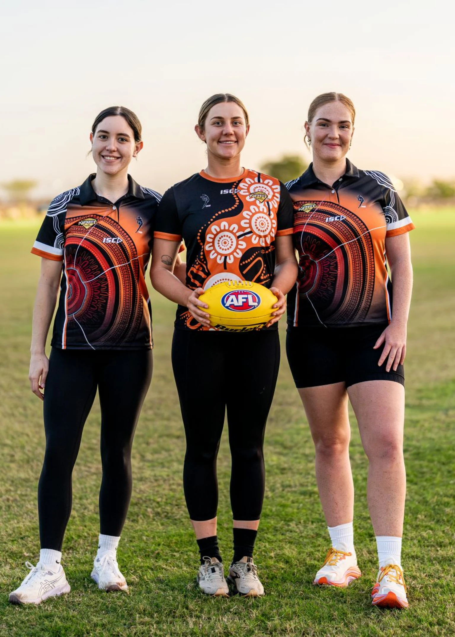 Three people standing on an oval holding a football