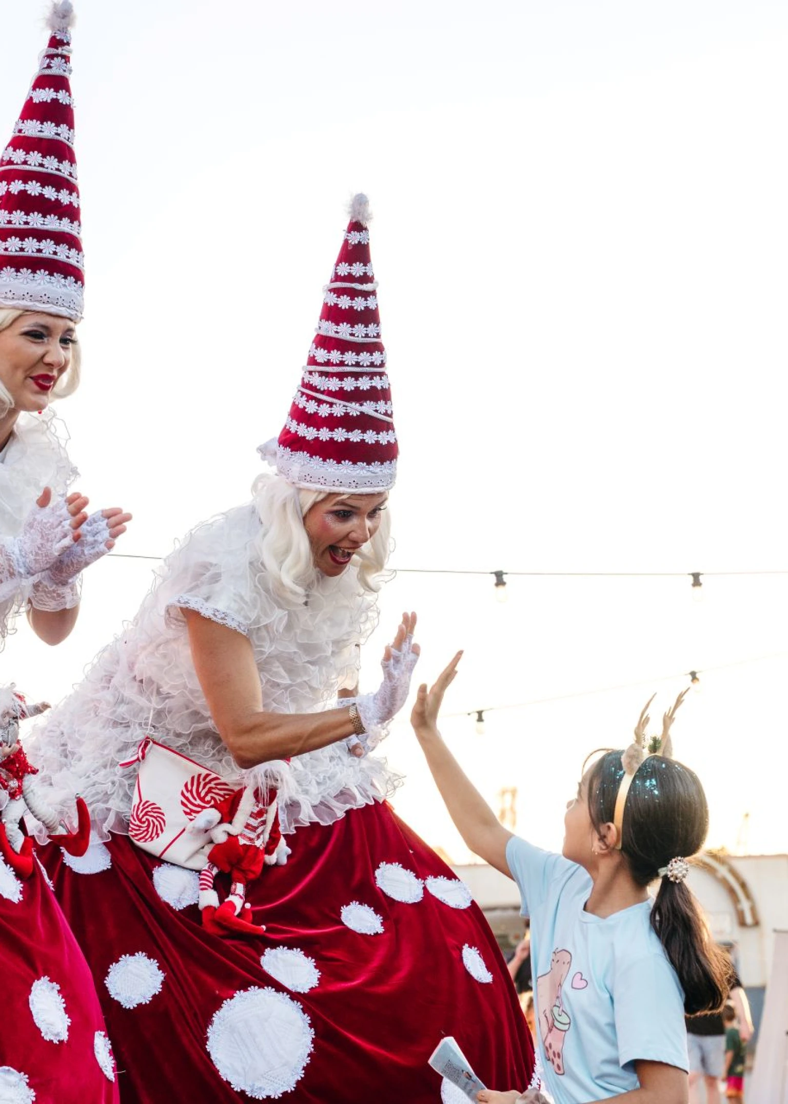 Duas pessoas em pernas de pau, vestidas com fantasias de Natal, dando um “high five” a um jovem